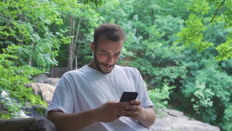 Texting-on-the-phone-at-the-waterfall-in-the-forest.